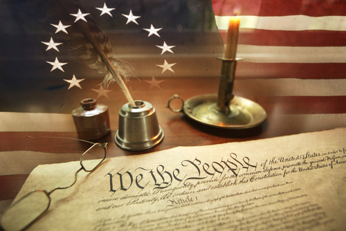 US Constitution with quill pen, ink, glasses, candle and flag with thirteen stars