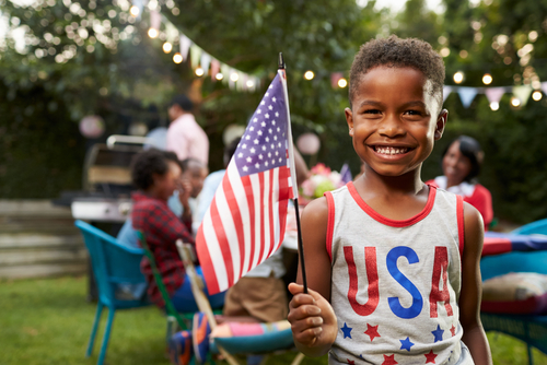 Young black boy holding flag at 4th July family garden party.