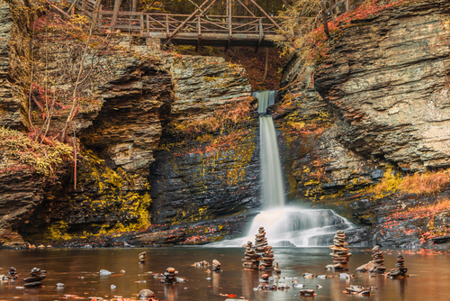 A footbridge and cairns surround Deer Leap Falls in peak fall foliage at Delaware Water Gap in Pocono Mountains, PA.