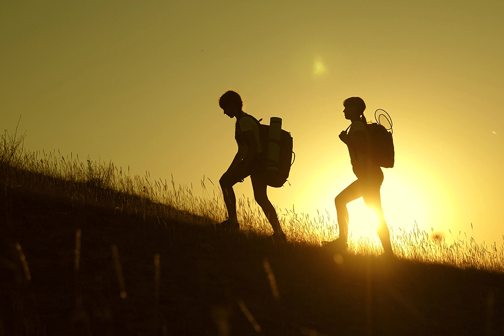 Children with backpacks climbing a mountain with the sunset in the background.