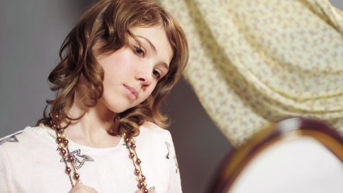 Girl wearing beads looking in the mirror.