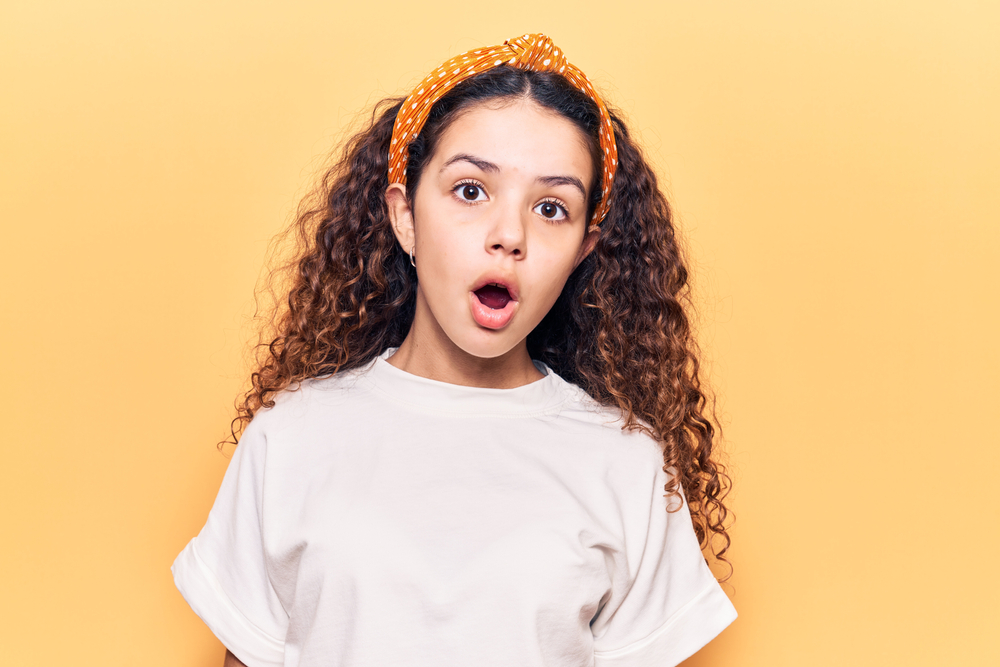 Young child with curly hair wearing casual clothes with an amazed look on their face.