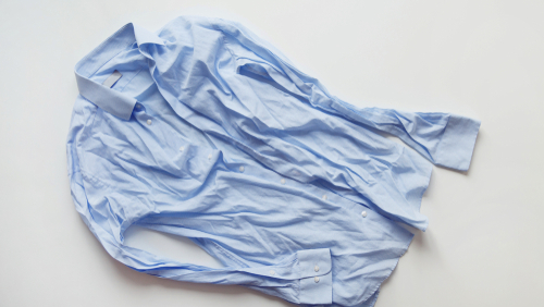Blue cotton wrinkled and rumpled shirt on white. Washed shirt after tumble dryer.