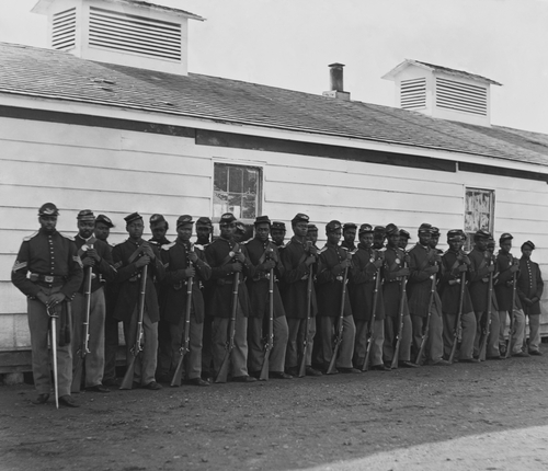 Company E, 4th U.S. Colored Infantry, were part of the defending forces of Washington, D.C. Photo shows two rows of African Americans holding rifles at Fort Lincoln in 1864.