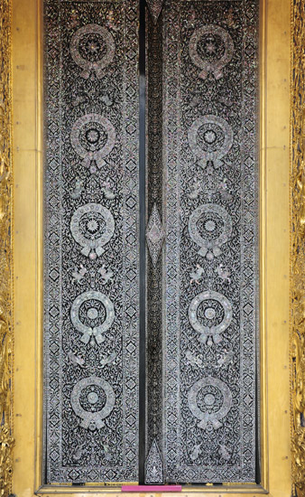 This is a window from a Thai temple. There is an intricate pattern that repeats on the front of the door.
