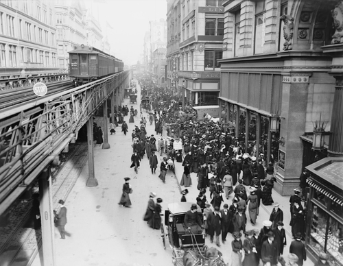 New York City's Sixth Avenue crowded with shoppers in 1903. Horse drawn carriages and wagons travel on the street level as an elevated train passes above.
