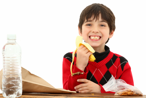 Attractive 7 year old french american boy in school desk over white eating a sack lunch or snack.