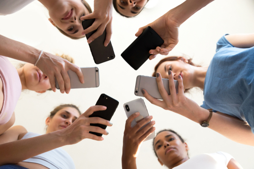 Diverse young women standing together in circle holding smartphones.