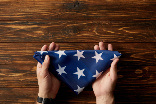 cropped shot of man holding folded american flag on wooden background