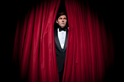 man standing between stage curtains