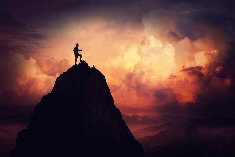 Man climbing a tall mountain shrouded in clouds.