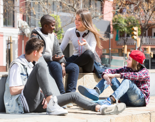 Teens spending time together and talking in sunny day in square.