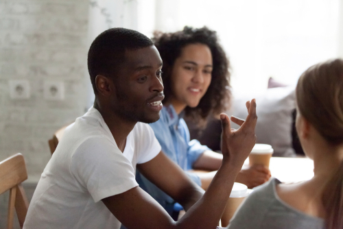Guy sitting at table in cafe, with diverse female friends talking, enjoying free time.
