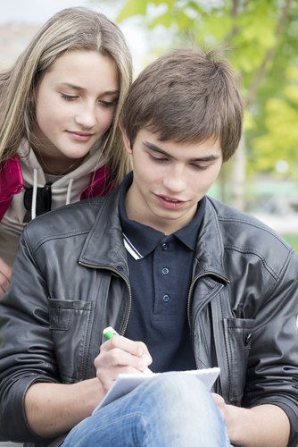 girl looking over shoulder of boy writing in notebook