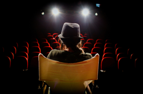 A young woman on director's chair on stage in front of empty seats.