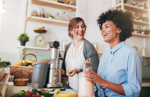 Two young women talking and smiling while working at bar counter.
