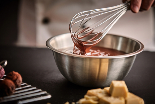 Chef holding a whisk with melted chocolate over a mixing bowl in the kitchen.