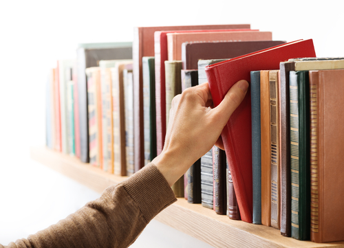 A person selecting a red book from a bookshelf