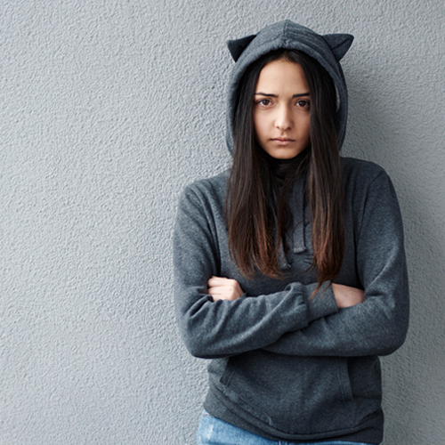 A girl in hood with cat's ears crossing her arms looking at the camera.