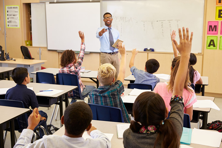 Kids raising hands to answer in an elementary school class.