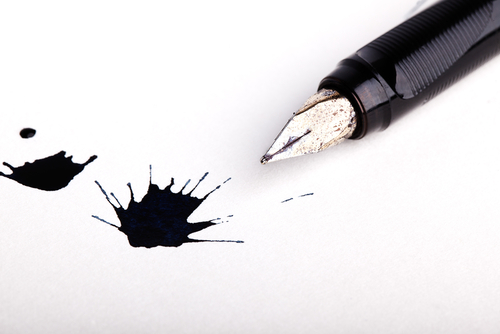 Ink splotches on white paper next to a pen