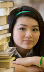 Young girl smiling next to a stack of books.