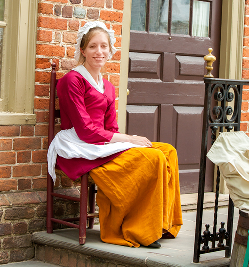 Williamsburg, Virginia, USA - 6/23/2009: A woman dressed in period clothing is sitting in front of the millinery shop in colonial Williamsburg.