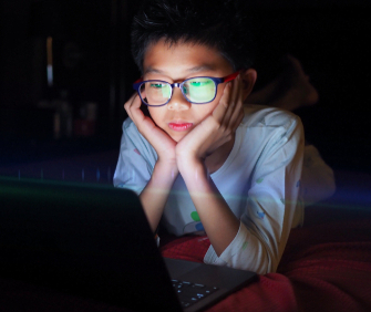 Boy lying in bed and watching laptop at night.