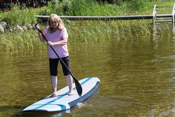 Older Adult woman uses a stand up paddleboard in a shallow area of a lake