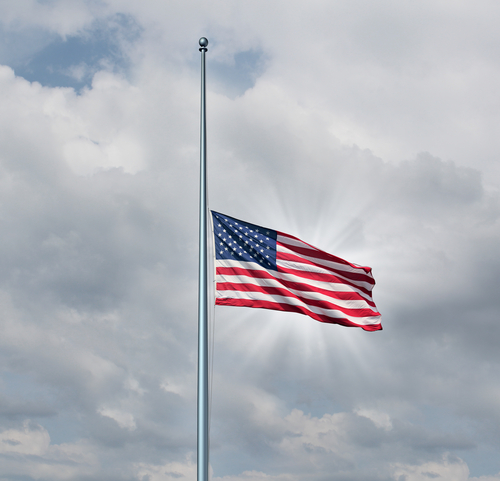 Half mast American flag concept as a symbol of the United States flying at low level on the flagpole on a cloudy day with a sun glow as an icon of honor respect and mourning for fallen heroes.