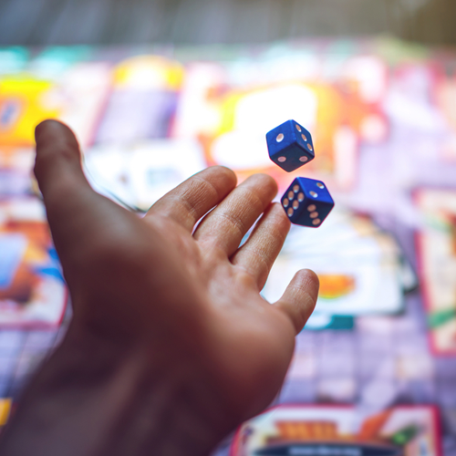 Hand throws the dice on the background of colorful blurred fantasy Board games, gaming moments in dynamics.