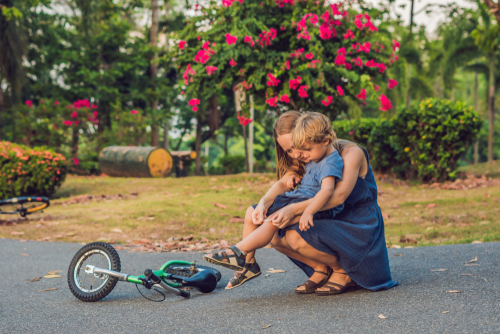 The boy fell off the bicycle, his mother pastes a plaster on his knee