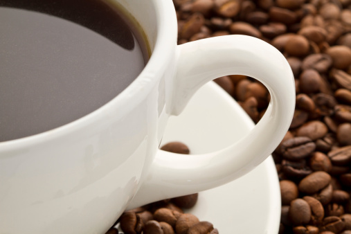 A white mug filled with coffee with coffee beans in the background. 