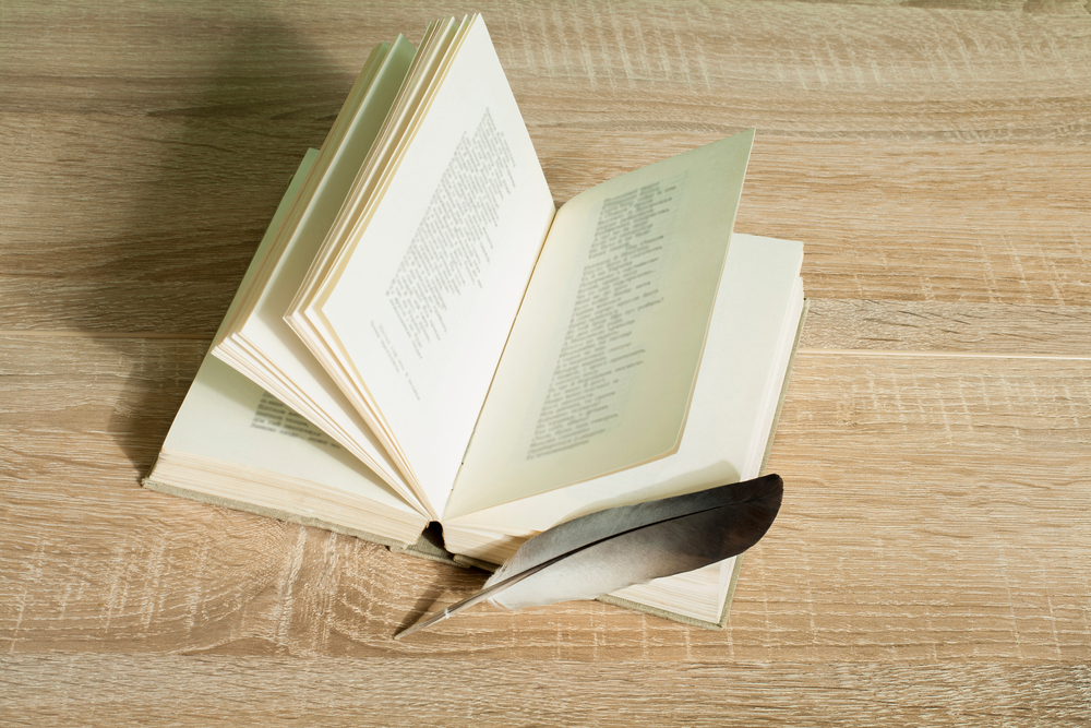 Book and feather quill pen on a wooden background.