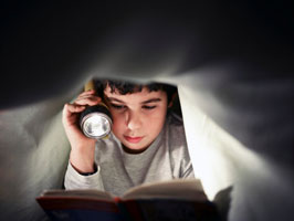 boy reading by flashlight in bed