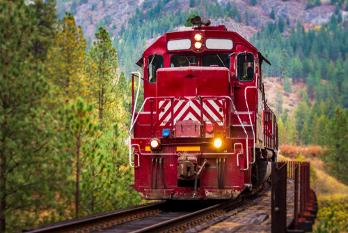 A large red and white locomotive thunders past , crossing over an old, weathered trestle