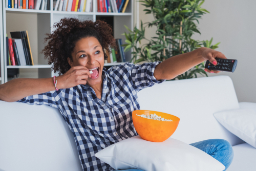 Woman watching tv at home and holding a remote control.