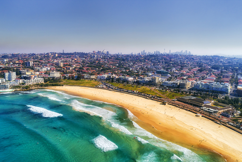 Wave breaks and surf on clear sand of famous Australian Sydney Bondi beach in aerial view with city