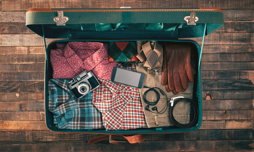 Suitcase packed with clothing, a camera, a smartphone, and earbuds.