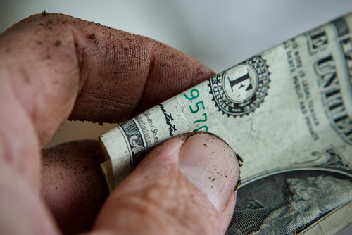 Man's hand covered in dirt, holding a dollar bill close up.