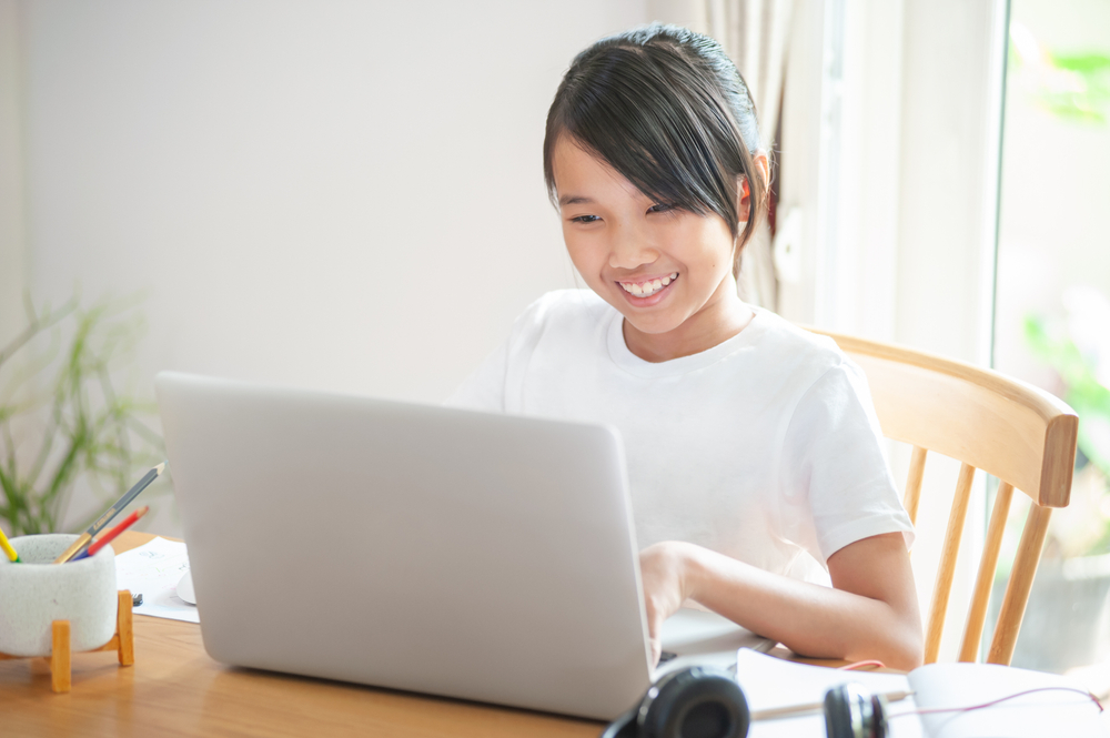 Smiling student using their laptop and learning online at home.