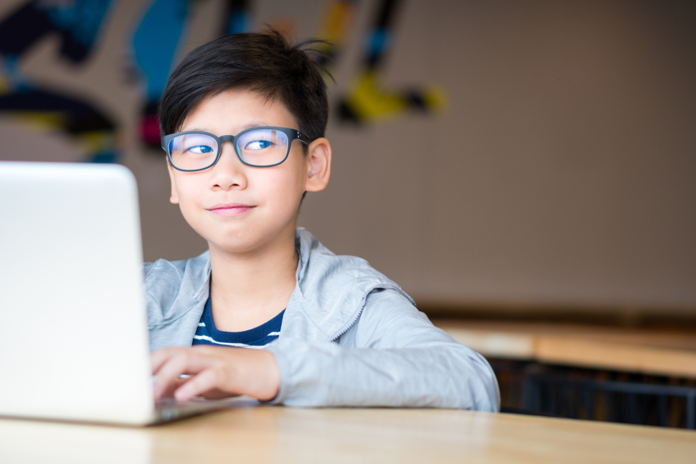 Boy happily using a laptop computer to study online lessons.