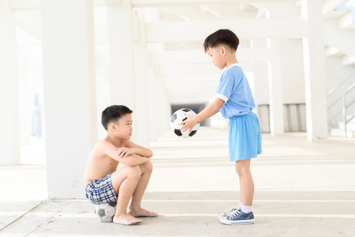 Young Asian boy give football to another boy in white building.