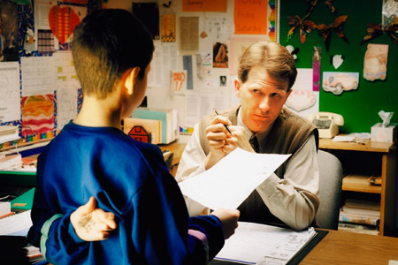 student with fingers crossed behind back talking with his teacher