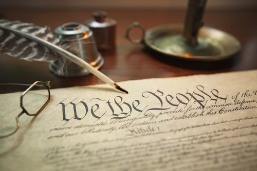 Selective focus image of the United States Constitution with quill pen, glasses and candle holder