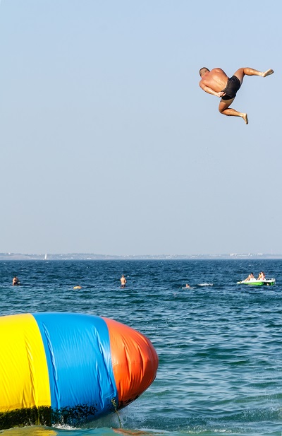 Young man is jumping with inflatable water catapult balloon on the sea shore