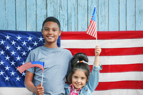Boy and small girl with American flags on wooden background