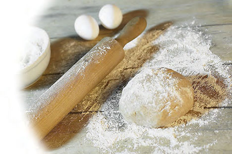 a rolling pin beside some flour, eggs and dough