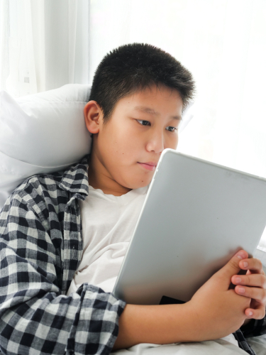 Happy Asian preteen boy using tablet on bed, lifestyle concept. 