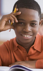 Young boy smiling at his desk with a pencil and a notebook.